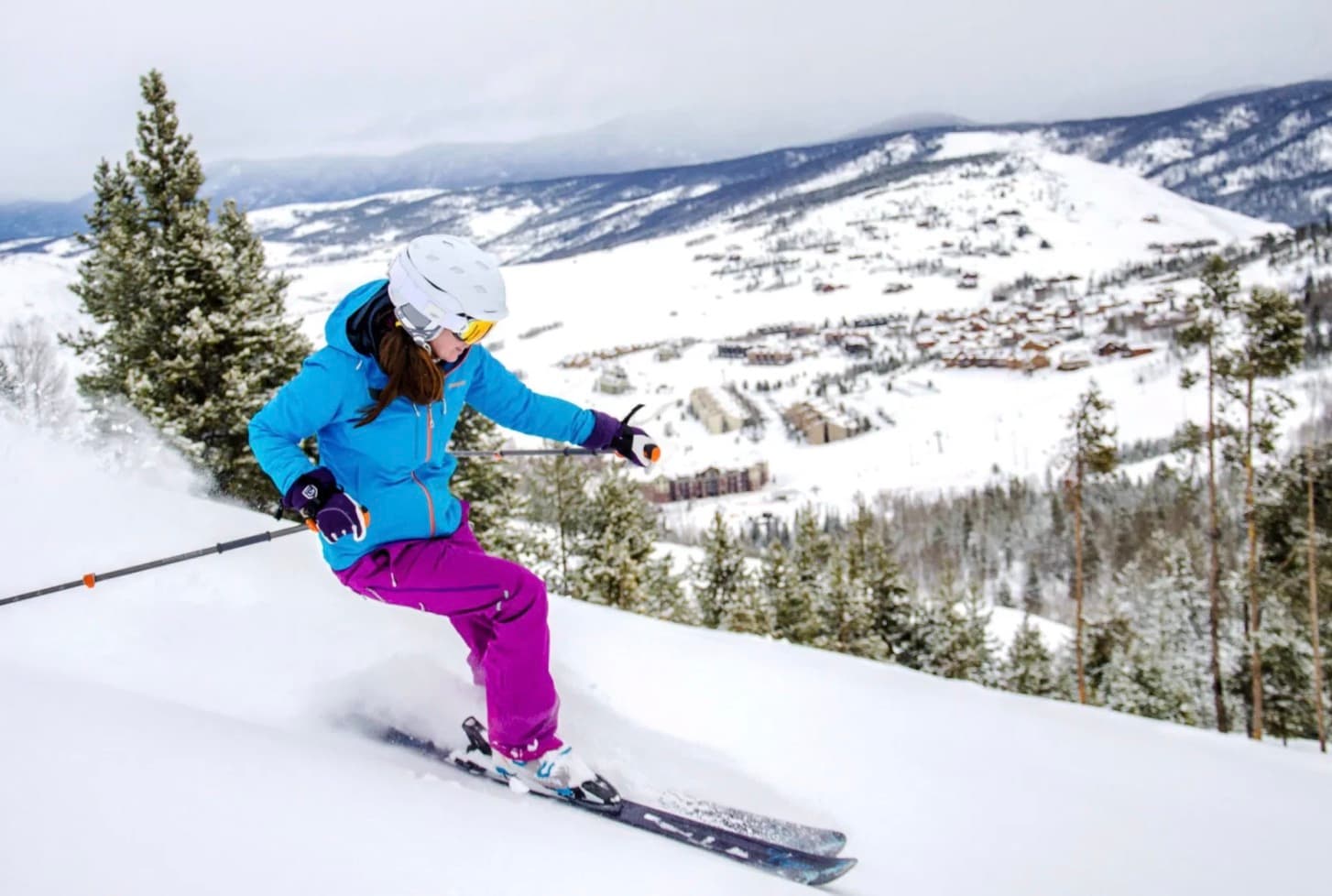 Skier carving a turn on a slope above a mountain resort village