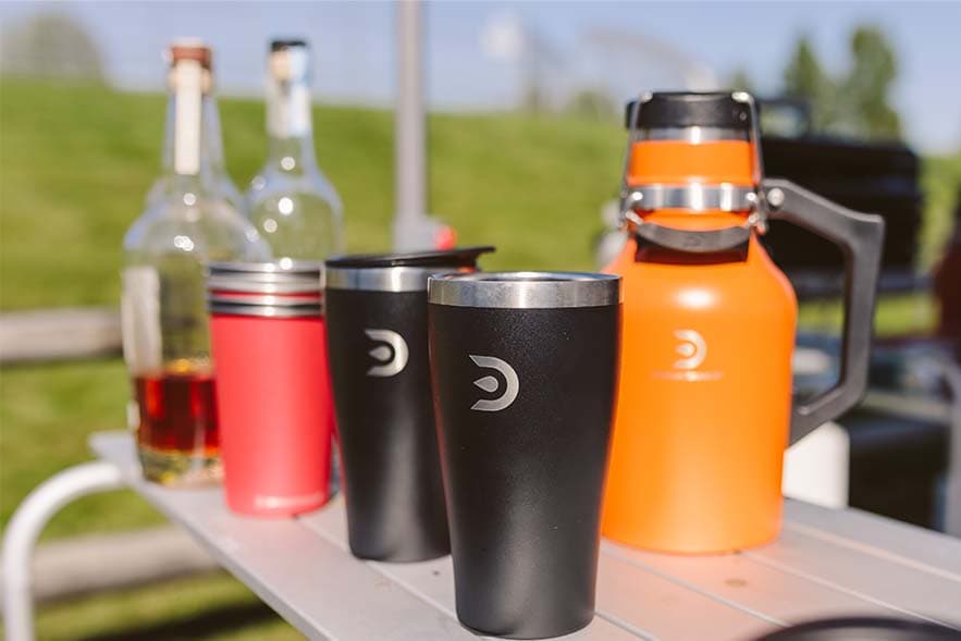 DrinkTanks tumblers and an orange growler lined up on an outdoor table