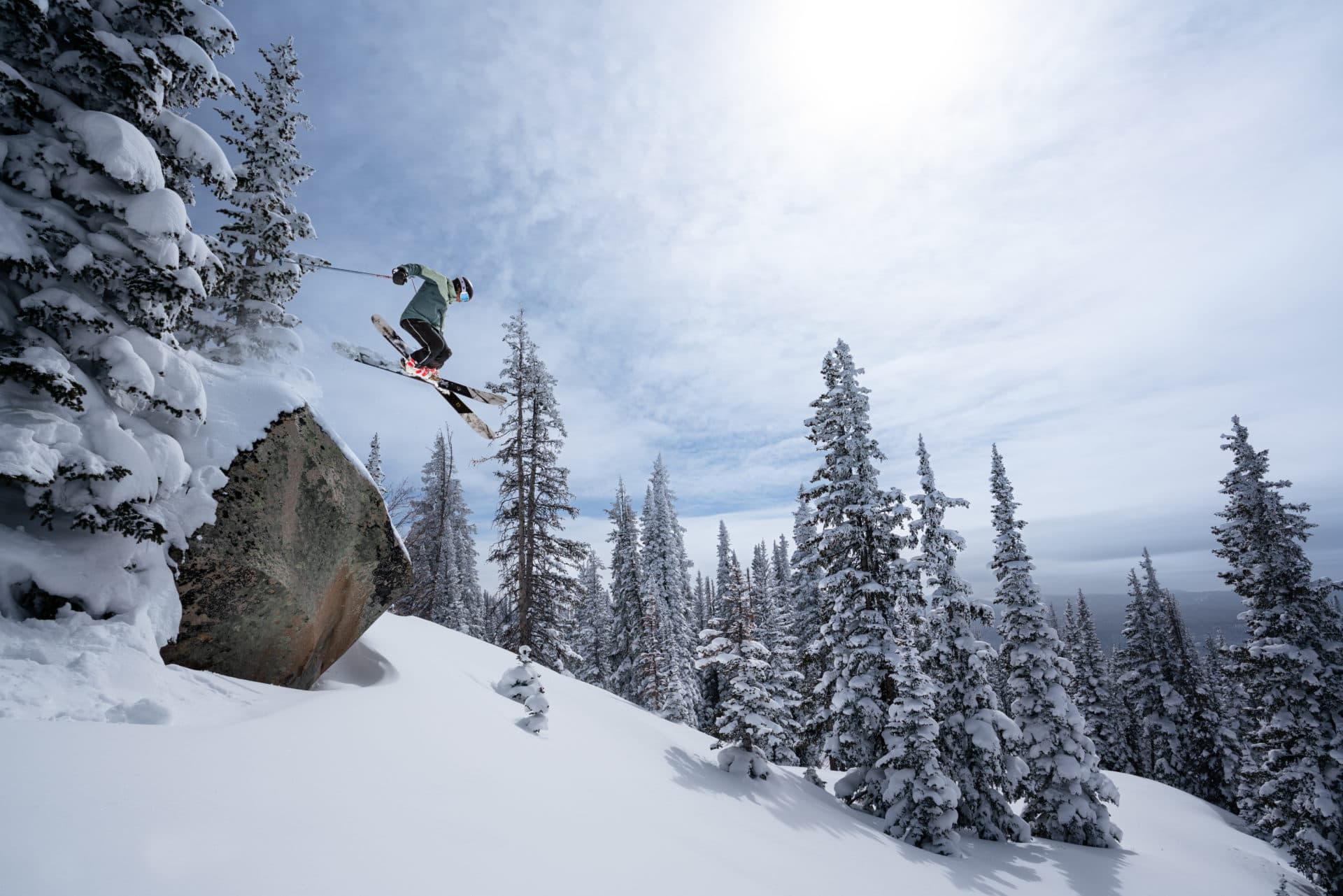 Skier launches off a snowy cliff ledge above an evergreen forest