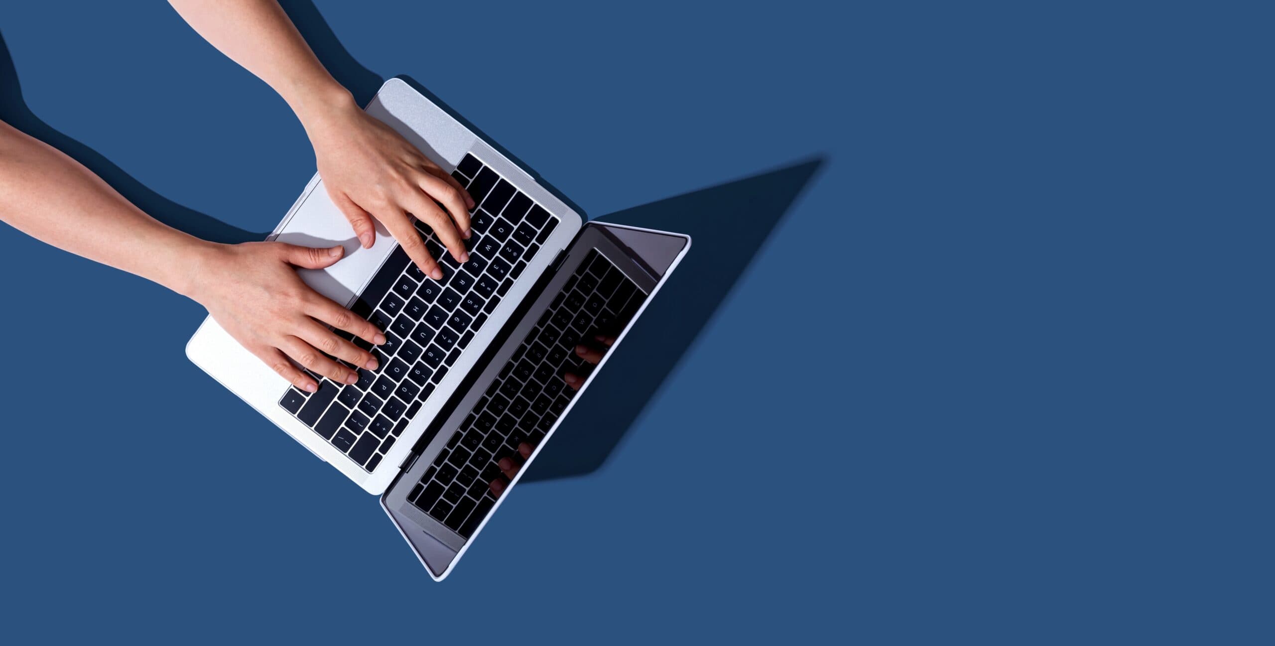Hands typing on a laptop keyboard against a blue background