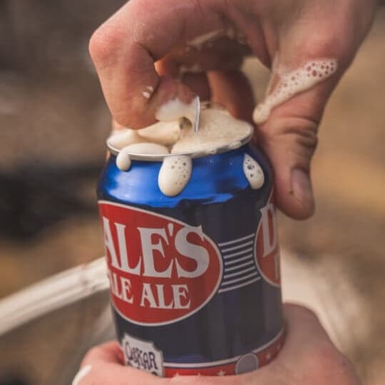 Hand opening a foaming can of Dale's Pale Ale outdoors