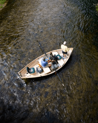 Aerial view of two anglers fly fishing from a wooden drift boat on a river