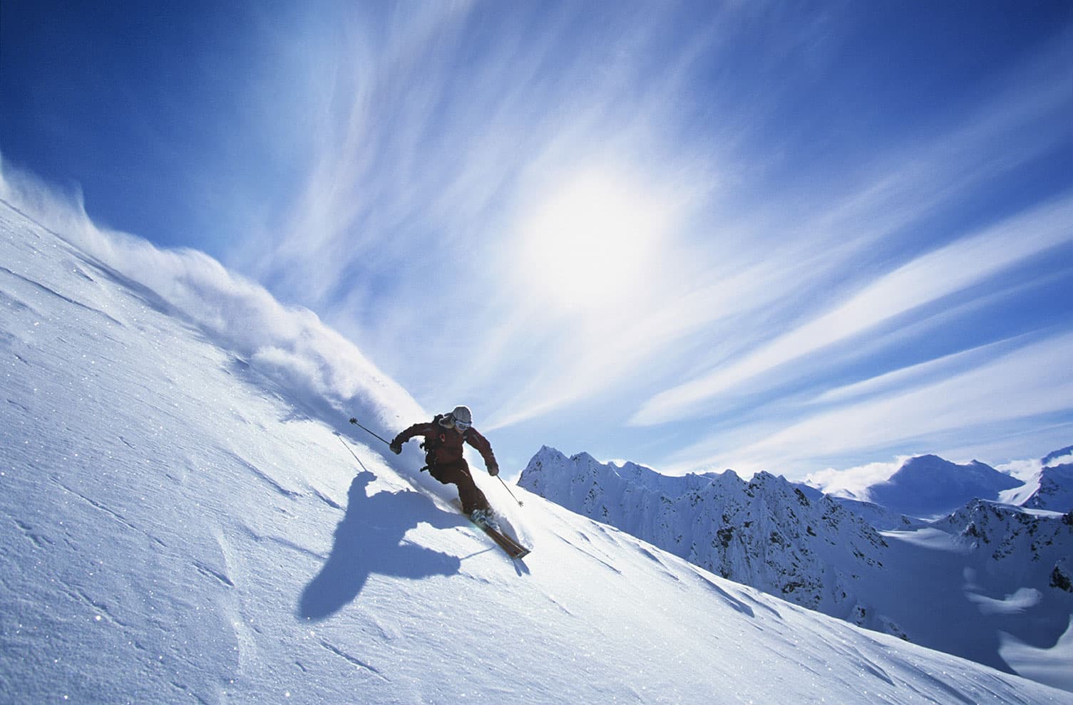 Skier carving through deep powder snow on a sunlit mountain slope