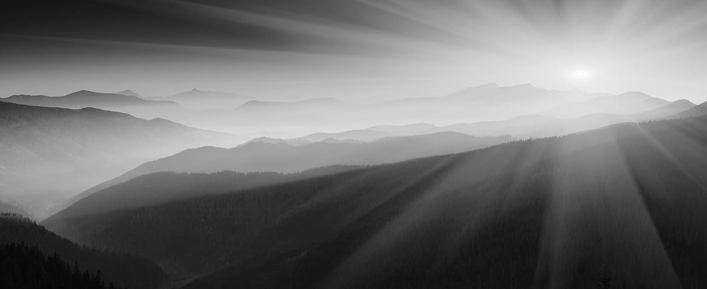 Black-and-white panoramic view of layered mountain ridges under radiating sun rays