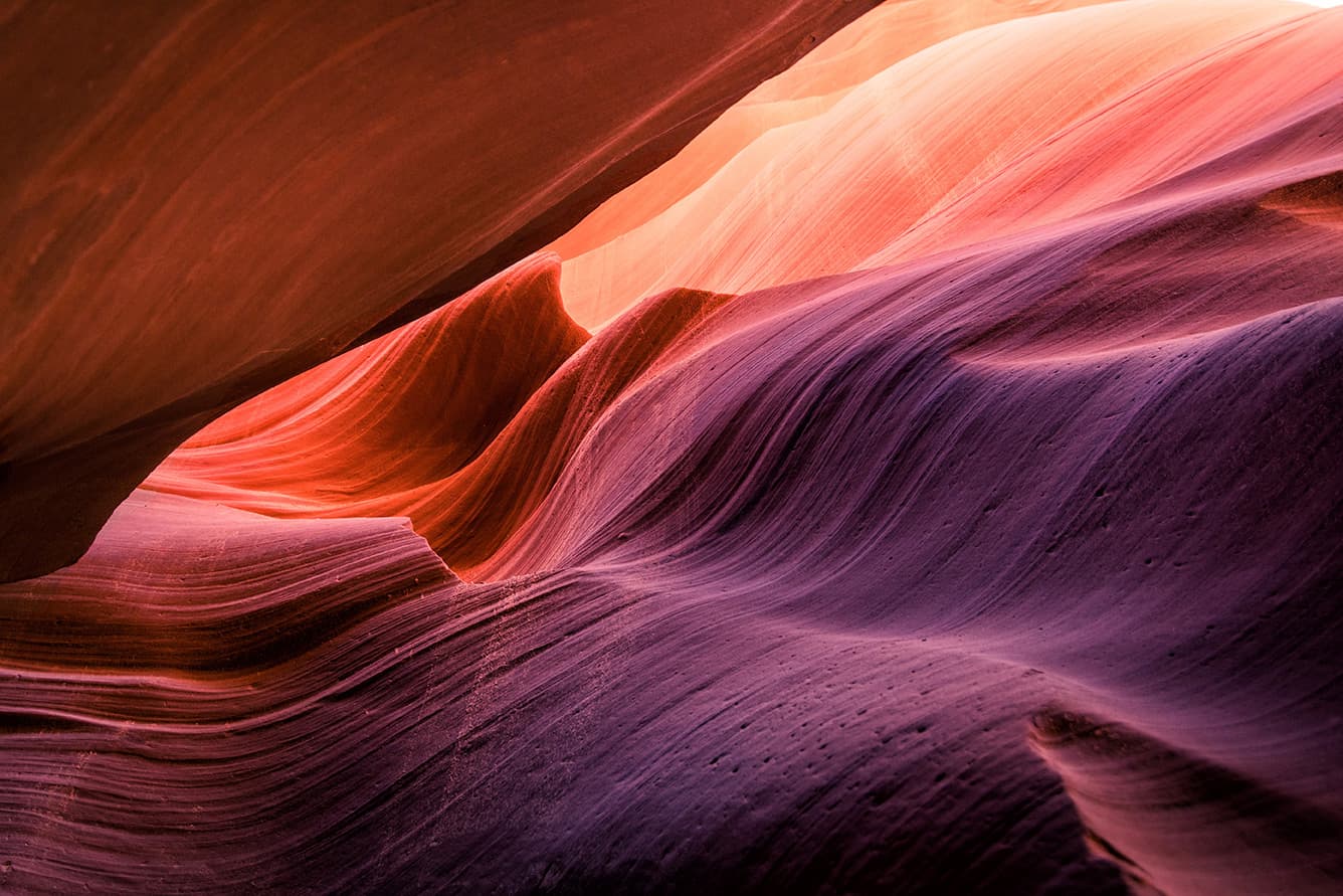 Sunlit sandstone slot canyon walls in warm orange and purple tones