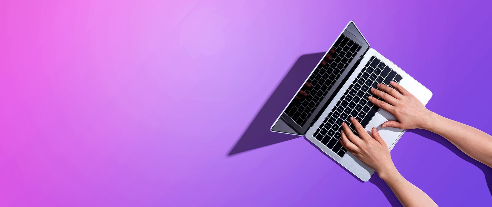 Overhead view of hands typing on a laptop against a purple gradient backdrop