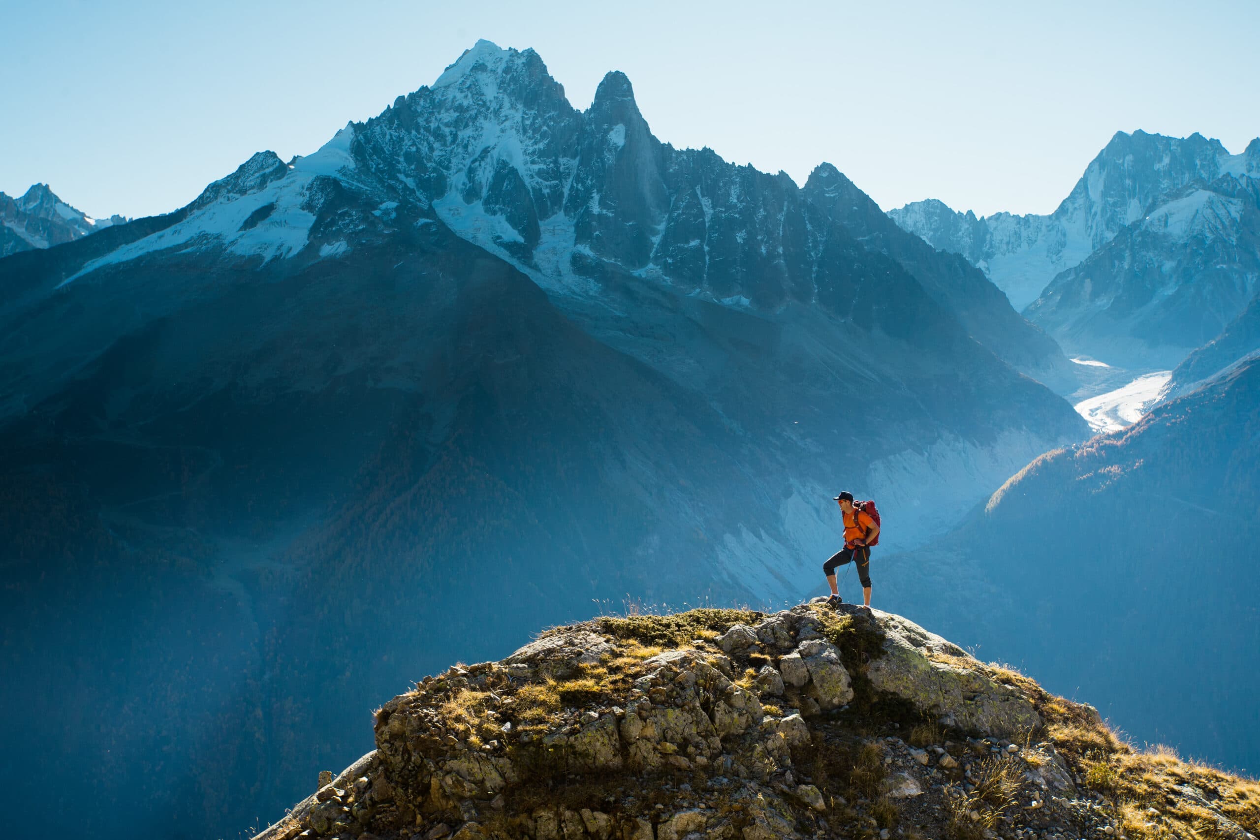 Hiker standing on a rocky summit overlooking snow-capped Alps peaks
