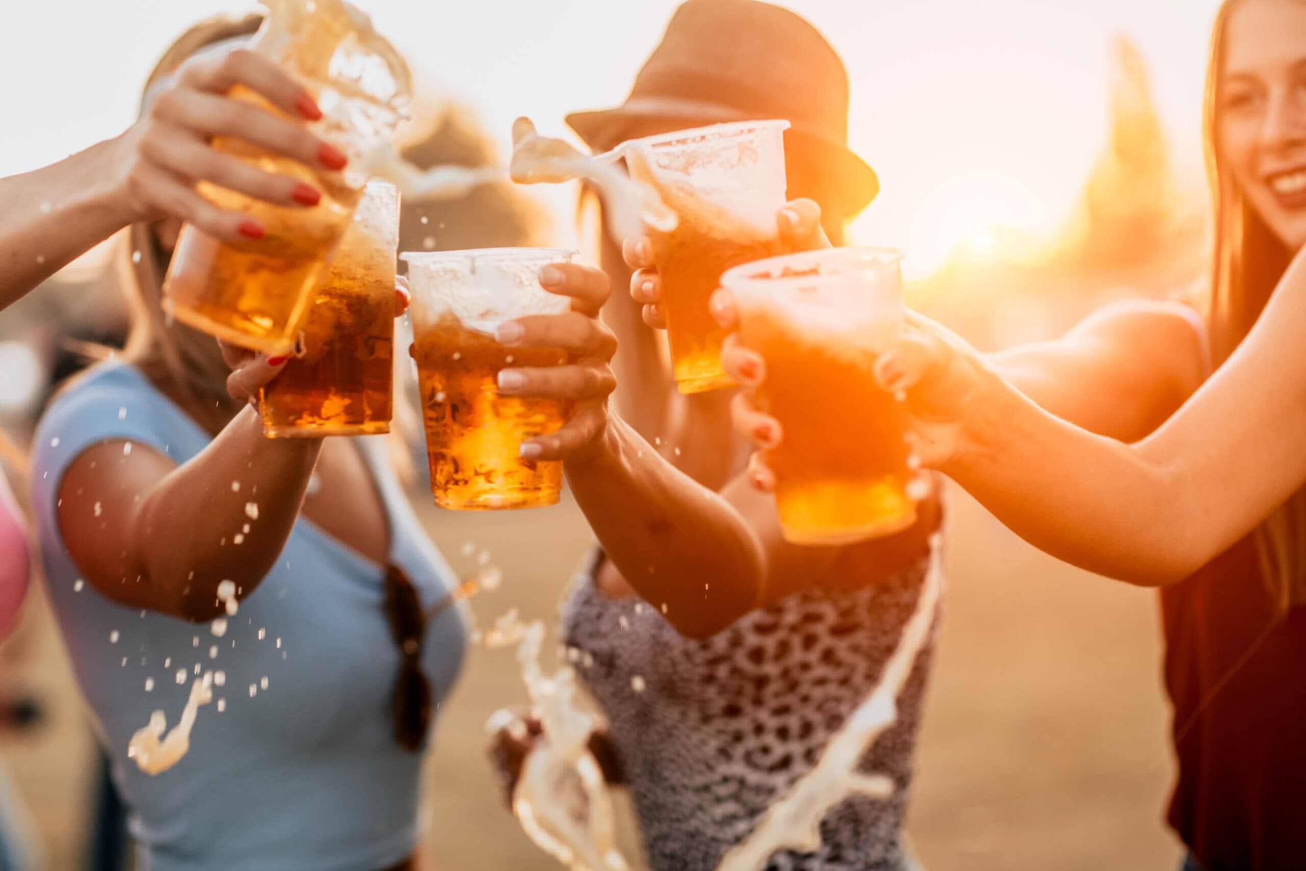 Friends toasting overflowing beer cups outdoors at golden hour