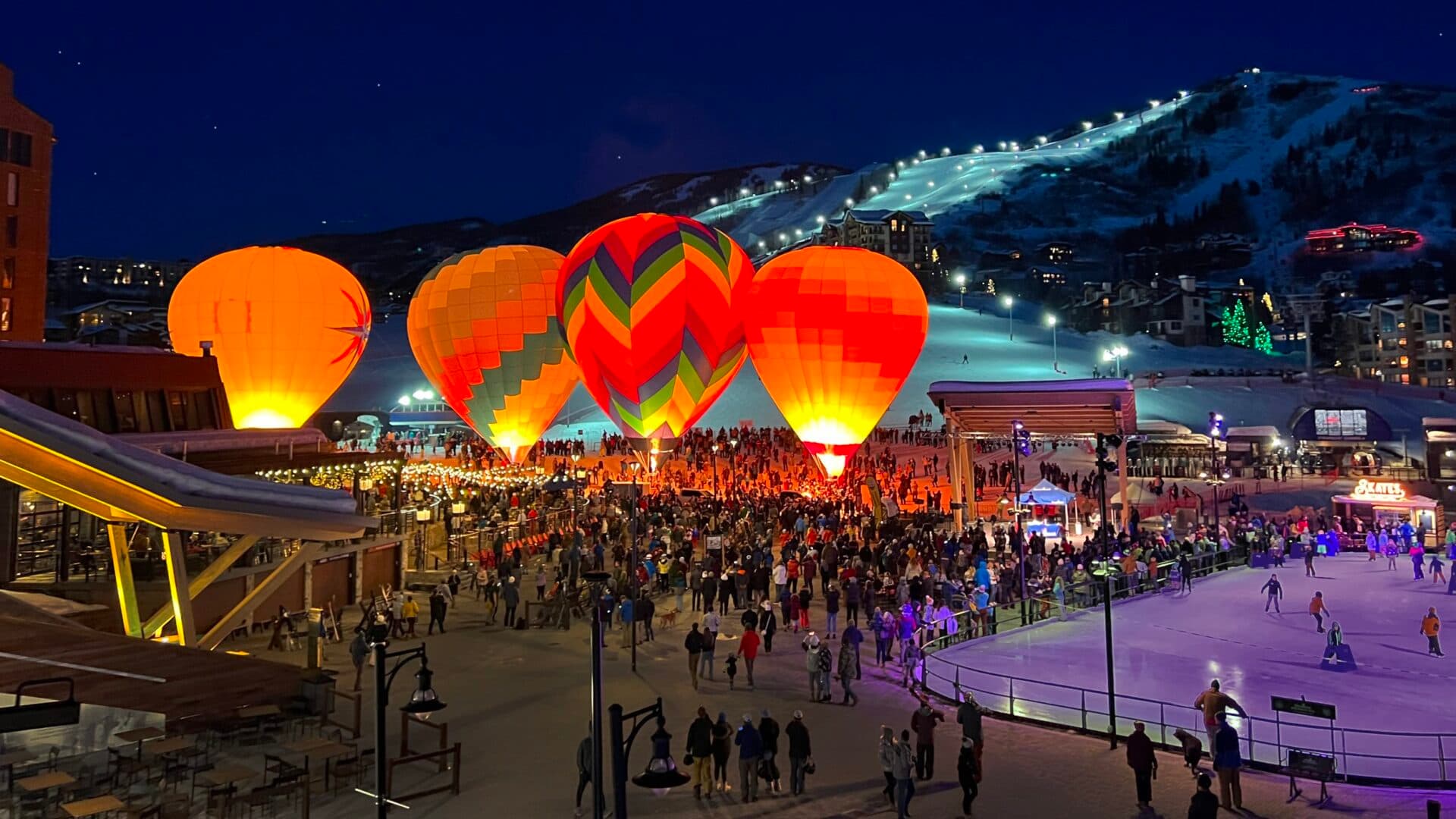 Hot air balloons glowing at night above a crowded Steamboat ski resort plaza