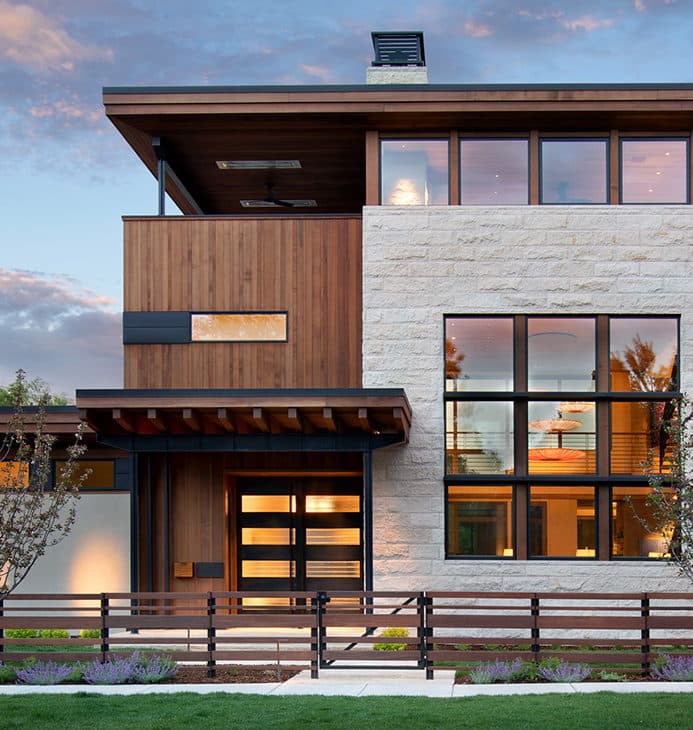 Modern home exterior with stone and wood siding lit at dusk.