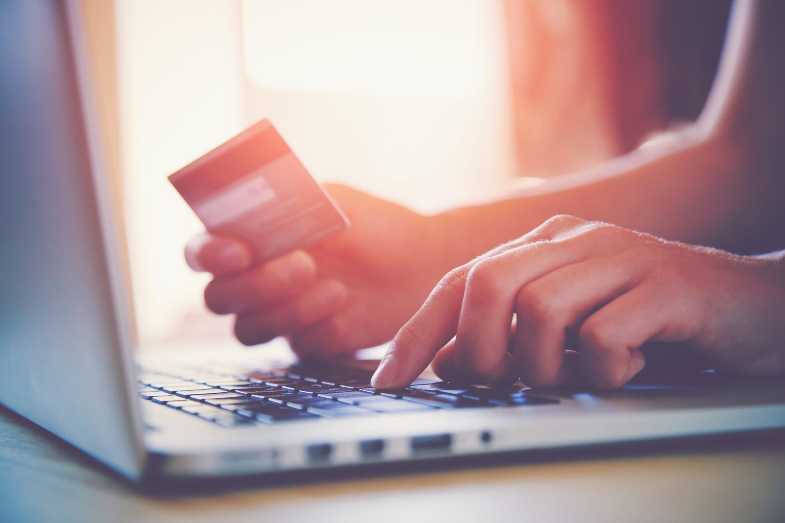 Person holding a credit card while typing on a laptop keyboard