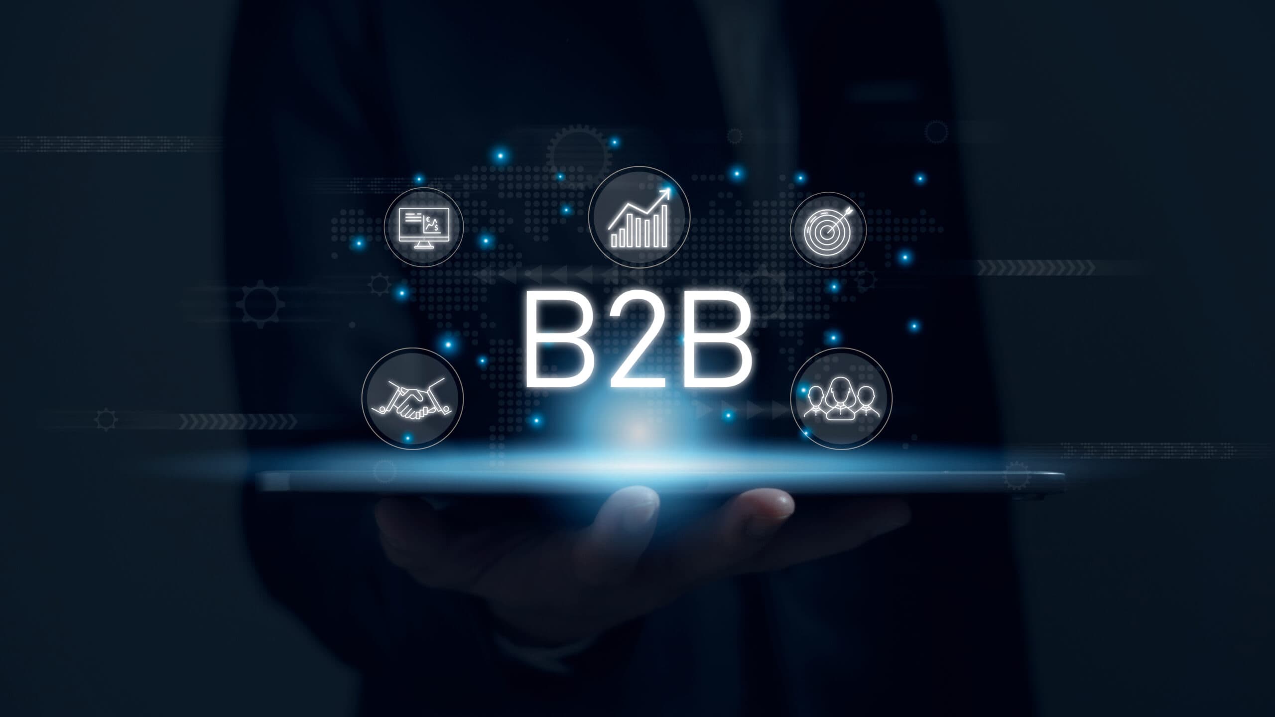 Hand holding tablet displaying holographic 'B2B' text and business icons