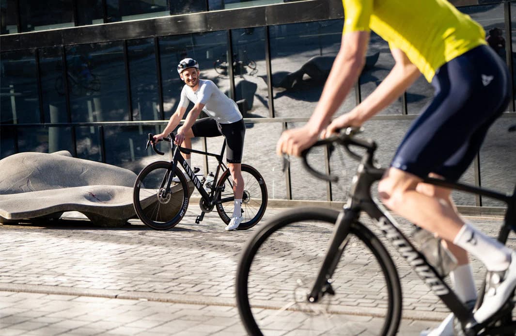 Cyclists riding road bikes through a paved urban plaza with modern buildings