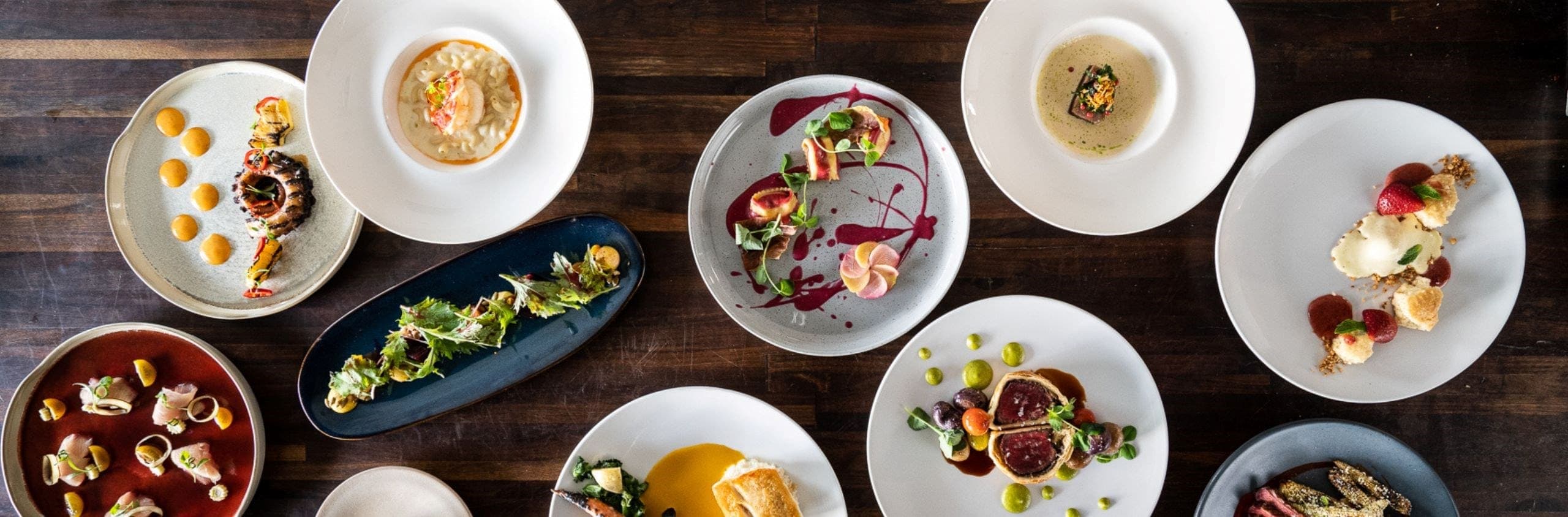 Variety of gourmet plated dishes arranged overhead on a wooden table