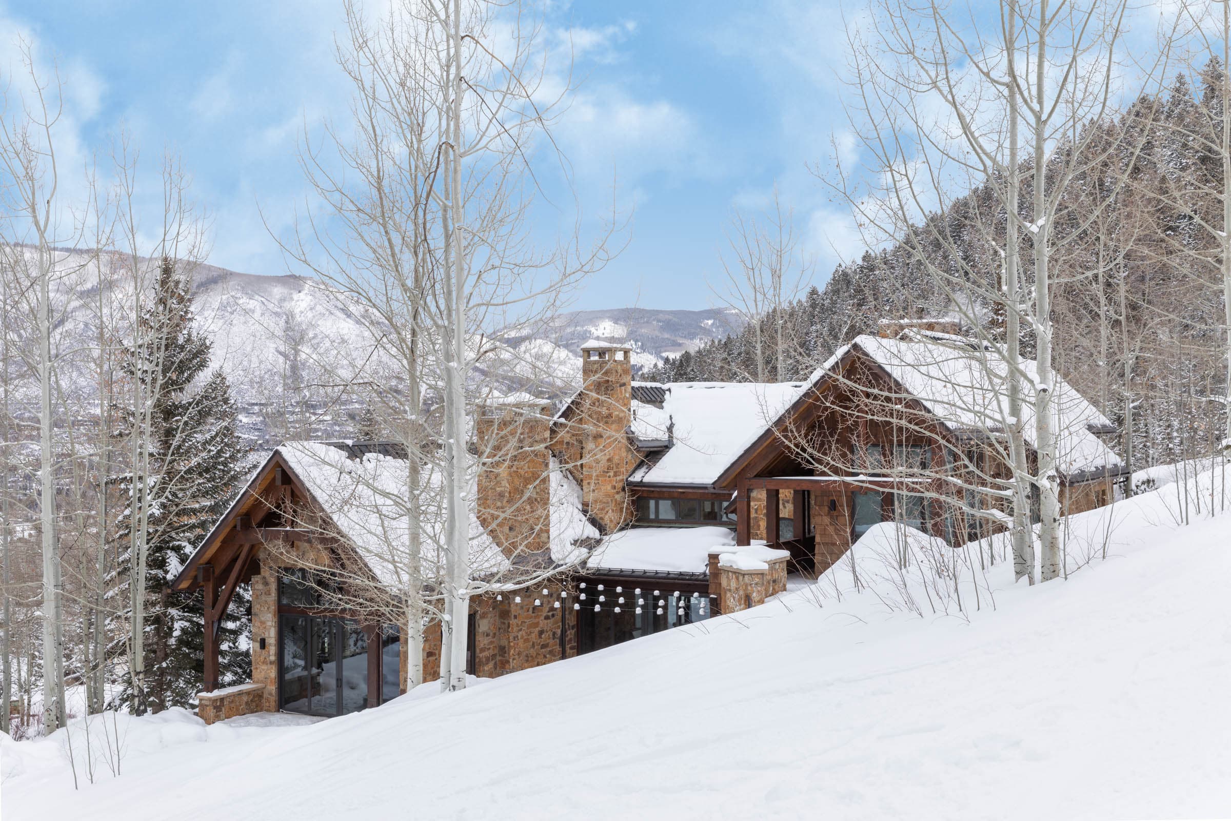 Timber-and-stone mountain home surrounded by snow-covered aspen trees